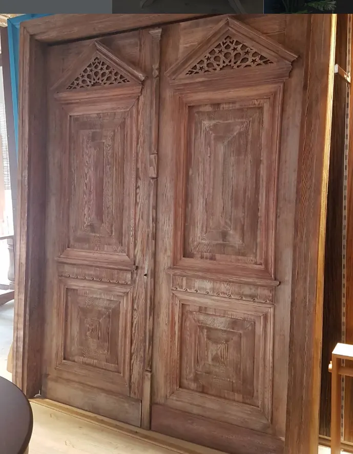 Weathered solid wood double door with carved panels and star-pattern fretwork pediments
