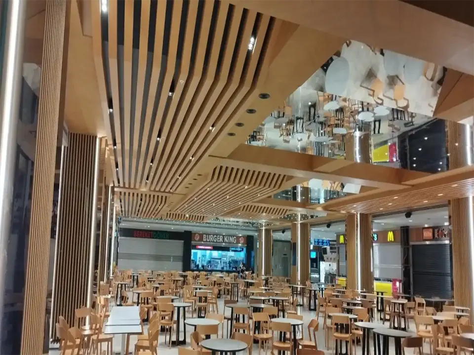 Converging lines of wooden ceiling slats over white tables in the food court