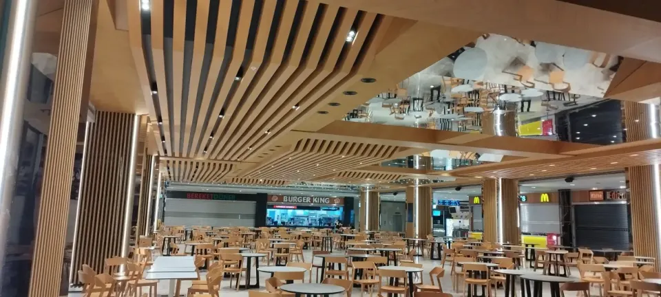 Wavy wooden slats stretching across a wide food court ceiling above slat-clad columns