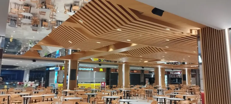 Layered wooden slatted ceiling beside a mirror panel over a wide table layout