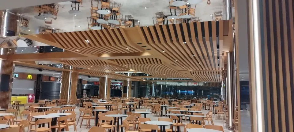 Rows of tables beneath wavy wooden slats and a mirrored ceiling surface
