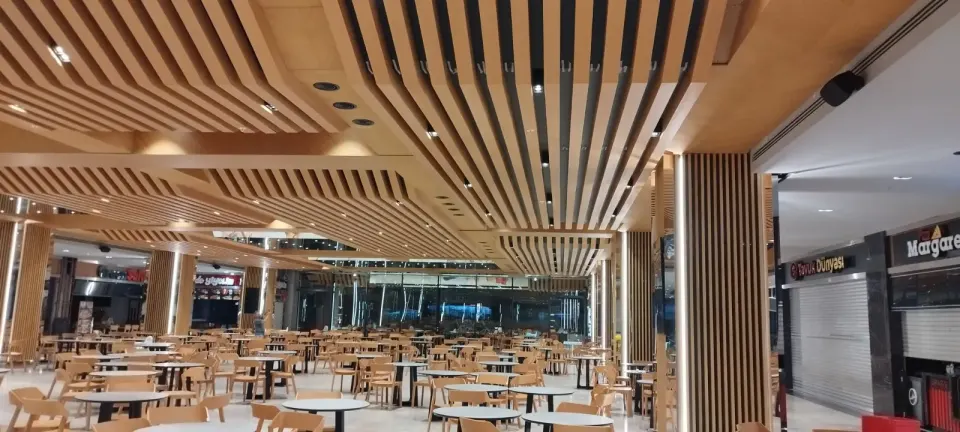 Empty tables in front of shop shutters under spotlit ceiling slats and a clad column