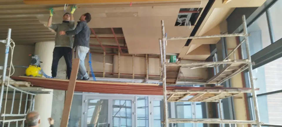 Two installers on scaffolding fitting ceiling panels while a colleague watches below
