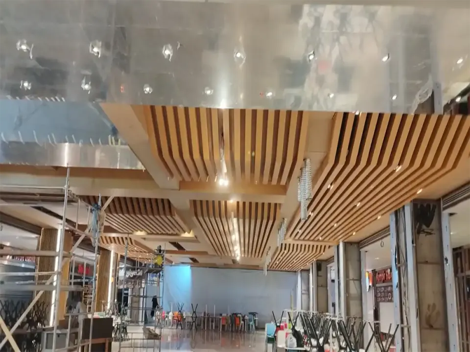 Food court under construction with hanging wooden slats, scaffolding and stacked chairs